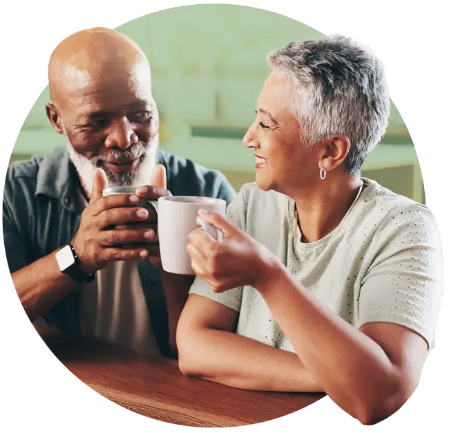 Photo of an older man and older woman smiling at each other as they drink coffee
